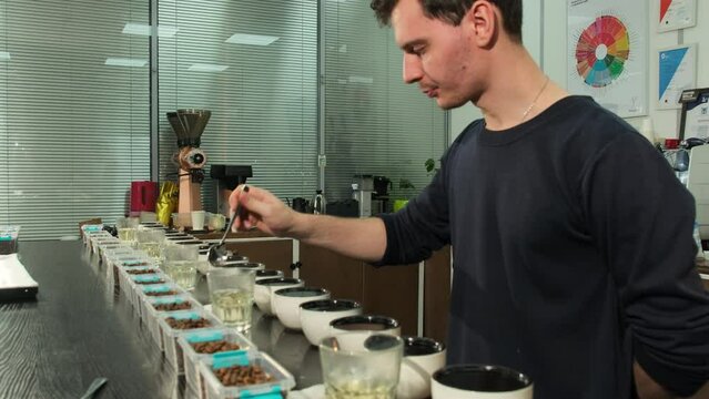 Skilled barista samples coffee using spoon during tasting session. Inspector dips spoon into boiling water before each subsequent cup