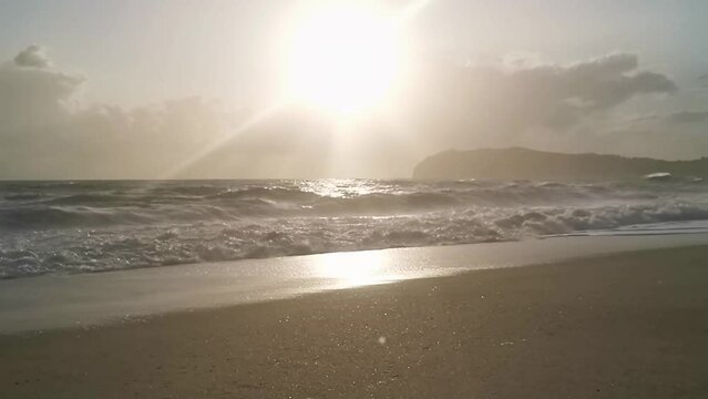 Luce dorata su una spiaggia solitaria al rallentatore con il mare agitato e Capo Palinuro sullo sfondo