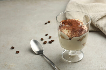 Delicious tiramisu in glass, spoon and scattered coffee beans on light table