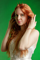 Portrait of a red-haired young woman with a crown on her head on a emerald background - 767260153