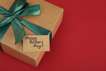 Happy Father's Day. Gift box and card with greetings on red background, closeup. Space for text