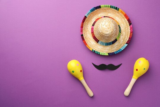 Mexican sombrero hat, fake mustache and maracas on purple background, flat lay. Space for text