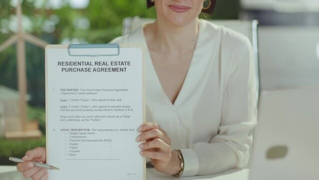 Sustainable real estate business. smiling elegant female realtor in modern green office in white blouse with clipboard and document.