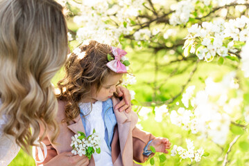A mother with a cute little daughter near a blooming pear tree in a meadow