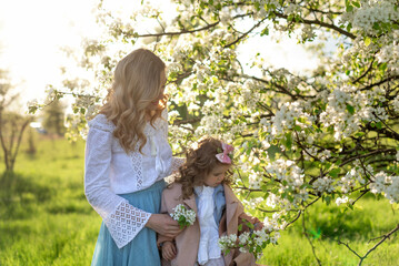 A mother with a cute little daughter near a blooming pear tree in a meadow