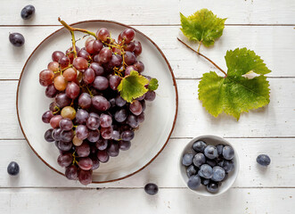 A plate of grapes and a bowl of blueberries are on a wooden table