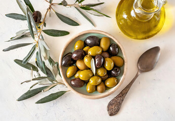 A bowl of olives and a spoon are on a table. The bowl is filled with green and black olives - Powered by Adobe