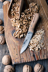 Crushed walnut nuts kernels and knife on wooden plate close up. Food photography - 767275583