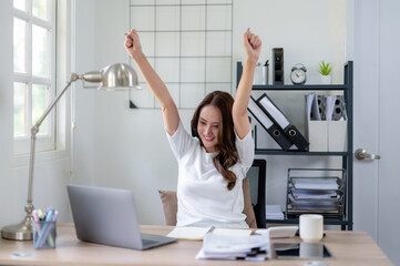 Cheerful businesswoman celebrates a successful moment while working at her desk in home office.