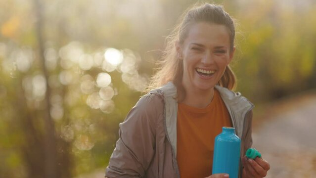 Hello autumn. happy stylish 40 years old woman in fitness clothes in the park with bottle of water.