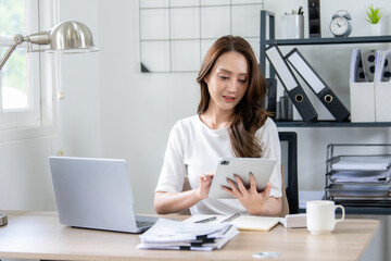 A smiling professional woman multitasking with a tablet and laptop in home office.