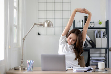 A young woman stretches her arms above her head, enjoying a moment of relaxation at home office.