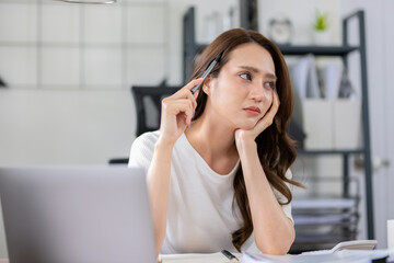 Obraz premium Businesswoman looks stressed, bored and holding her head. Indicates a headache while working at a desk in home office.