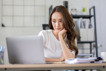 Businesswoman looks stressed, bored and holding her head. Indicates a headache while working at a desk in home office.