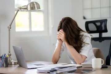 A businesswoman appears stressed and experiencing a headache while focusing on her work in home...