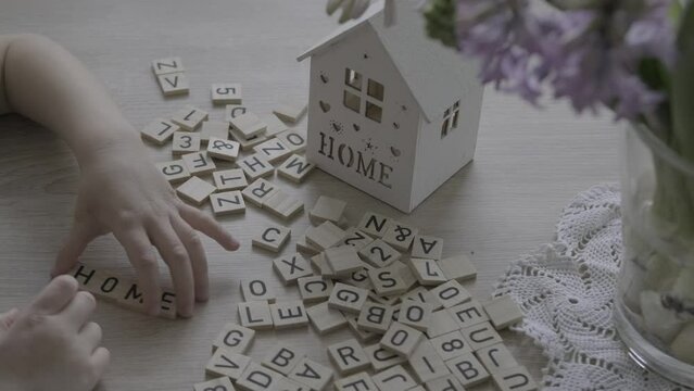 small child 4 years old playing with wooden alphabet blocks, makes up word home from letters, house model, concept home mortgage, home insurance, exploring English language