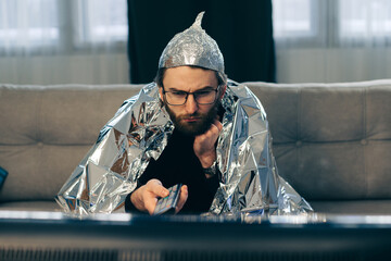 A man in a tinfoil hat watches TV.