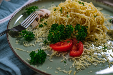 noodles spagetti with butter served with cheese, tomatoes , mushroom and parsley on table cloth, blue napkin, light green ceramic plate
