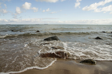 Fale rozbijające się o kamienie na piaszczystym brzegu morza Bałtyckiego