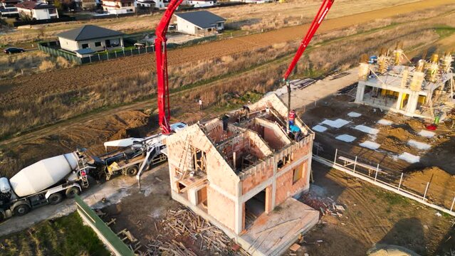 Aerial drone footage of a concrete boom pump truck pouring freshly mixed concrete on a new building. Slab building foundation casting. Cement mix laying on a new residence. Workers at height.
