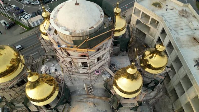 Aerial close up drone shot of the construction of an orthodox church with golden domes. Scaffold work on a brand new place of worship. gilded bell tower.