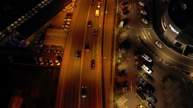 Aerial high angle shot of evening roads in a city bustling with cars commuting. Drone flyover footage of cityscape and vehicles driving along a road and over a bridge in an urban neighbourhood.
