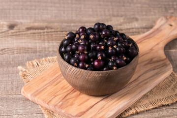 Black currant in a bowl on wooden background. Organic berries. 
