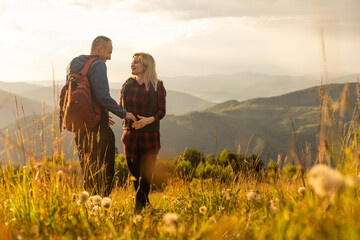 A man and a woman in tourist equipment are standing on a rock and admiring the panoramic view. A couple in love on a rock admires the beautiful views. A couple in love is traveling. A couple on a hike - obrazy, fototapety, plakaty