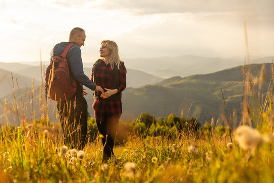 A man and a woman in tourist equipment are standing on a rock and admiring the panoramic view. A couple in love on a rock admires the beautiful views. A couple in love is traveling. A couple on a hike