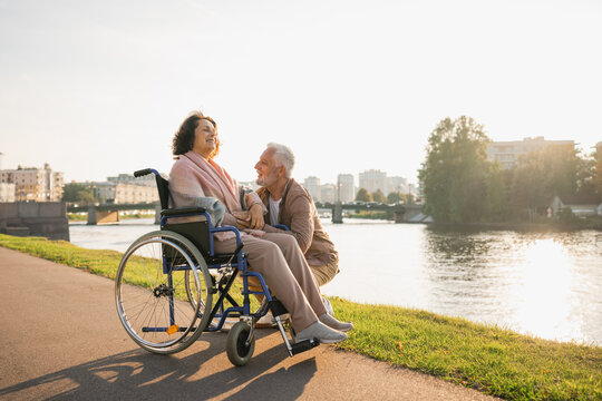 Senior woman in wheelchair walking with caregiver old man on road. Elderly family couple man supporting taking care of paralyzed woman in chair for people with disability outdoor. Rehabilitation - Powered by Adobe