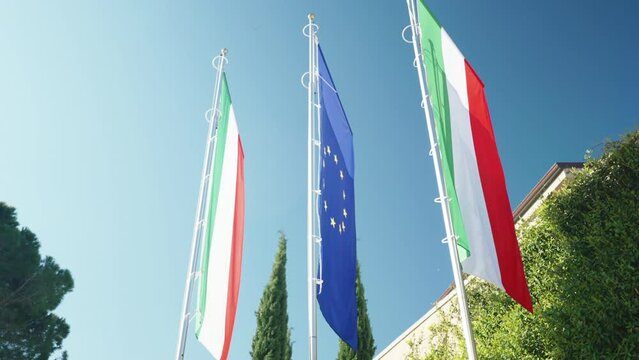 Flags of Italy and European Union against blue sky background, symbol of unity between the countries of Europe, democracy, financial agreements, trade and common currency concept