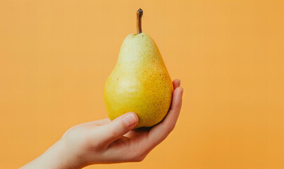 Hand holding pear on pastel orange background. Diet and healthy eating concept.