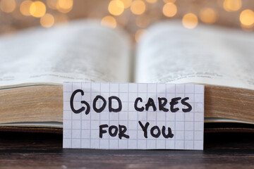 God cares for you, handwritten quote in front of open holy bible book with bokeh light background....
