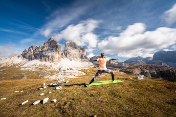 A woman practising yoga with the view to the monumental peak of Three Peaks of Lavaredo/Tre Cime di Lavaredo - obrazy, fototapety, plakaty