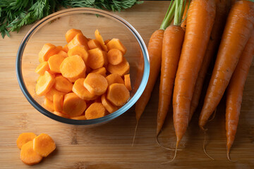 sliced carrots in a round glass bowl and whole carrots on the table