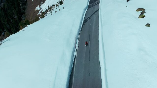 Static aerial shot of cyclist on professional carbon road bike in red winter jacket ride on an empty road with snow walls. Cycling in harsh conditions, winter training