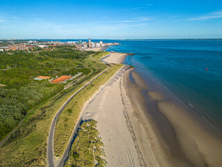 Aerial view of beach line and Vlissingen city, Netherlands in background, against blue sky

