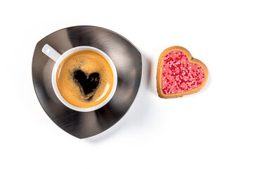 A cup of coffee on a saucer with one heart-shaped cookie in pink glaze. Top view on a white...