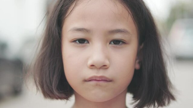 Face and eyes closed up 4K of adorable Asian kid girl who is looking and staring outdoor with serious and concerned emotional expression shows concept of worried problem of z generation child.