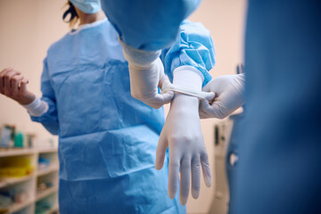 Close up of surgeon preparing for operating room with help of nurse.