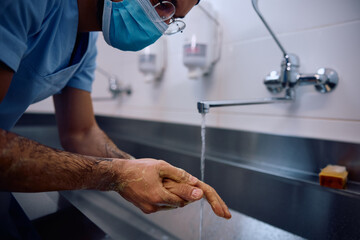 Close up of surgeon washing hands while preparing for operating room at clinic.