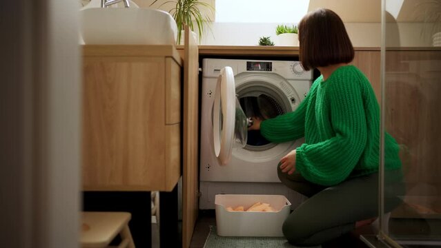 Domestic woman opening door of washing machine and removing clean clothes at house