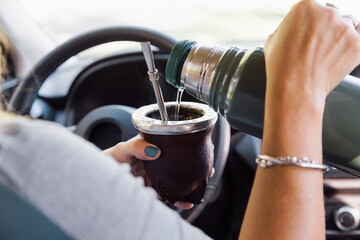 Woman sitting in a car pouring water to Yerba Mate from a thermos into a Mate cup.