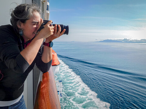 Woman takes pictures with digital camera of the natural views from a cruise ship.