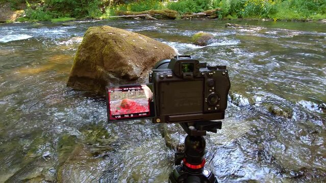 Dslr camera on a tripod captures serene water stream scenery in a lush forest setting