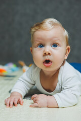 A four-month-old boy lies on the floor on a rug and plays with toys. The child holds his head. A baby learns to crawl on the floor