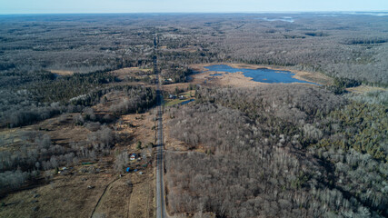 An aerial view of a road cutting through a forest with marshes and lakes in the distance