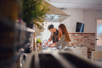 A man and woman washing dishes and glasses in a kitchen - obrazy, fototapety, plakaty