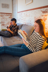 Obraz premium Young couple engaging in separate activities on a living room couch at home
