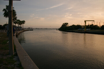 Fototapeta premium Leading lines Wide view south out of City of Gulfport Municipal Marina. Calm Blue Water with small Ripple waves. Curved seawall and boats in the background. With cloudy sky in Gulfport, FL. Sunset 